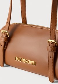 Καφέ τσάντα χειρός από συνθετικό δέρμα με κλείσιμο με φερμουάρ, εξαρτήματα σε χρυσή απόχρωση και ανάγλυφο λογότυπο "LOVE MOSCHINO" στο μπροστινό μέρος. Δύο ρυθμιζόμενα λουριά.
