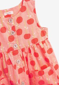 Korallinvärinen mekko punaisen omenan kuviolla, pyöreä kaula-aukko ja nappihius. Mukana kerätty vyötärö ja kaksi sivutaskua.