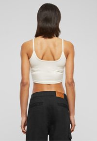 Débardeur crème court avec fines bretelles, associé à un pantalon noir avec une étiquette en cuir à l'arrière et deux poches arrière. Texture lisse.