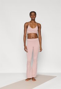 Σετ αθλητικής ένδυσης σε ανοιχτό ροζ χρώμα με εφαρμοστό αθλητικό σουτιέν που διαθέτει συγκεντρωμένη λεπτομέρεια και κολάν με φουσκωτό τελείωμα. Κατασκευασμένο από μαλακό, ελαστικό ύφασμα.