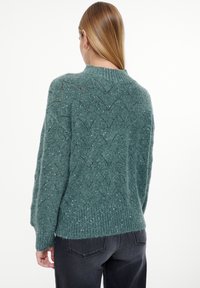 Groene gebreide trui met een getextureerd zigzagpatroon en metallic glitters, voorzien van een geribbelde zoom en een losse pasvorm. Achteraanzicht.