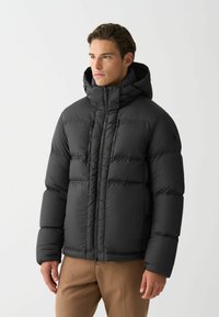Jachetă puffer neagră cu glugă, având un design matlasat, fermoar frontal și două buzunare cu fermoar. Material neted și lucios, cu o croială structurată.