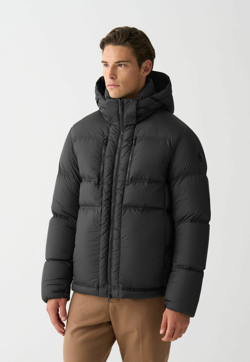 Jachetă puffer neagră cu glugă, având un design matlasat, fermoar frontal și două buzunare cu fermoar. Material neted și lucios, cu o croială structurată.