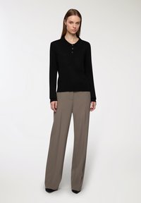 Czarny długi sweter polo z kołnierzykiem i trzema guzikami, zestawiony z jasnobrązowymi spodniami o szerokich nogawkach oraz czarnymi butami z wąskim noskiem.