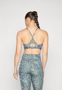 Sutiã desportivo em verde suave com um padrão animal texturizado. Apresenta alças cruzadas nas costas e um detalhe recortado. Combinado com leggings de cintura alta a condizer.