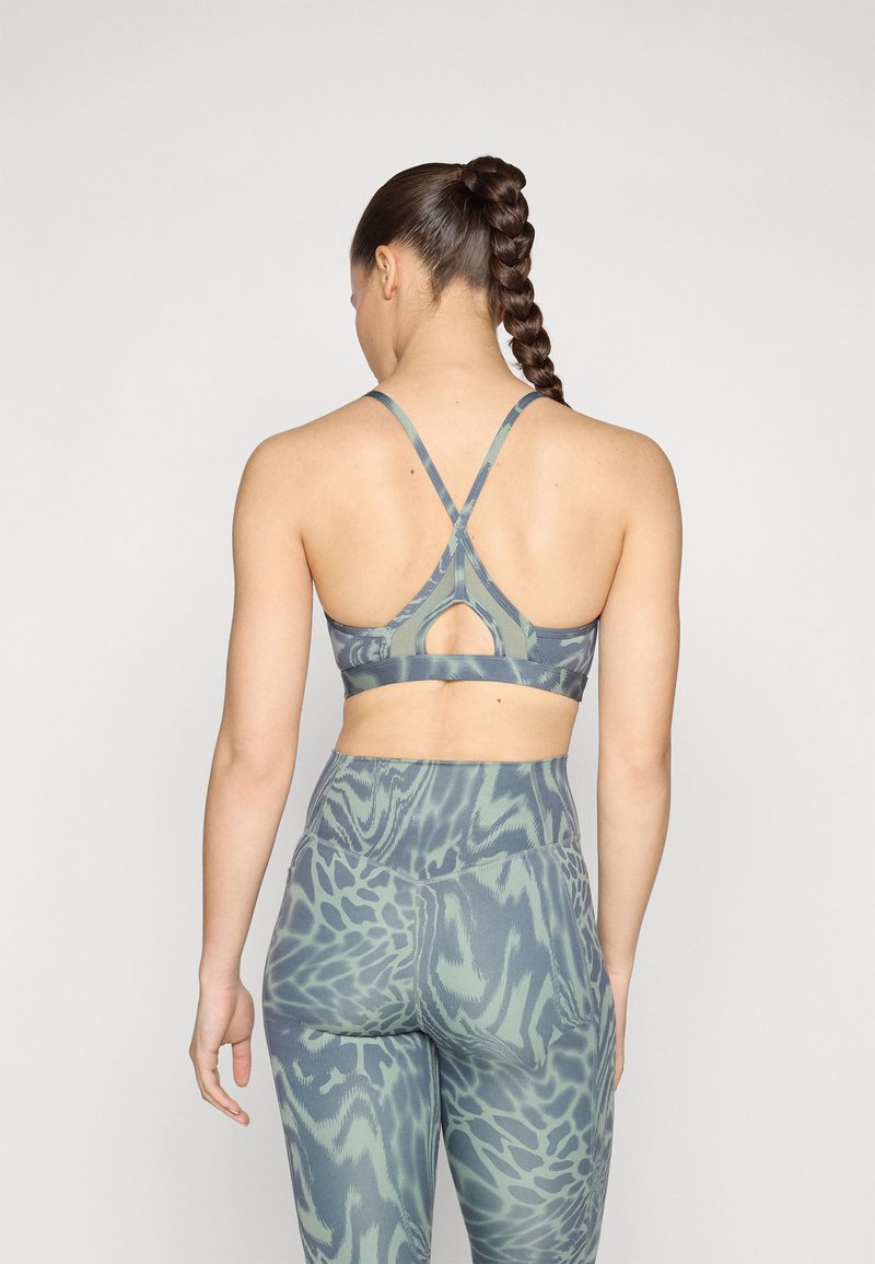 Sujetador deportivo en verde apagado con un estampado animal texturizado. Cuenta con tirantes cruzados en la parte posterior y un detalle de corte. Combinado con leggings de cintura alta a juego.
