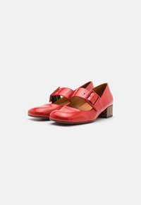 Pantofi Mary Jane din piele lăcuită roșie, cu vârful pătrat, având o curea largă cu detaliu de cataramă și un toc din lemn cu un model în zig-zag.