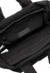 Borsa tote in tessuto nero con una tasca interna con zip e un'etichetta in pelle con logo. La borsa ha una consistenza morbida e maniglie robuste per il trasporto.