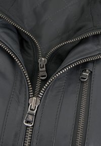Schwarze Lederjacke mit mehreren silbernen Reißverschlüssen an der Vorderseite, einem gesteppten Innenfutter und detaillierten Nähten.