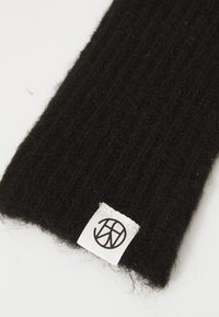 Tessuto a coste nero con un'etichetta bianca che mostra un logo circolare composto da linee e forme intersecate.