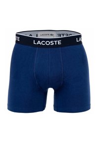 Sötétkék pamut boxer alsónadrág fekete rugalmas derékkal, amelyen fehér színben a "LACOSTE" logó szerepel. Simaság és testhezálló kialakítás jellemzi.