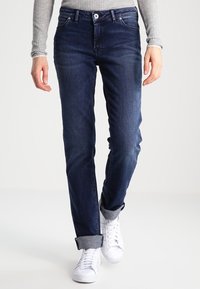 Mörka jeans i denim med rak benlösning, 5-fickors stil och uppvikta ärmar. Matchas med vita sneakers och en ribbad grå långärmad topp.