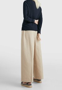 Haut à manches longues bleu marine, pantalon large beige ample avec une finition texturée, et espadrilles noires avec bordure blanche.