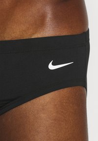 Svart svømmebokser laget av elastisk materiale med en hvit Nike-logo på venstre side. Har rene linjer og en tettsittende passform.