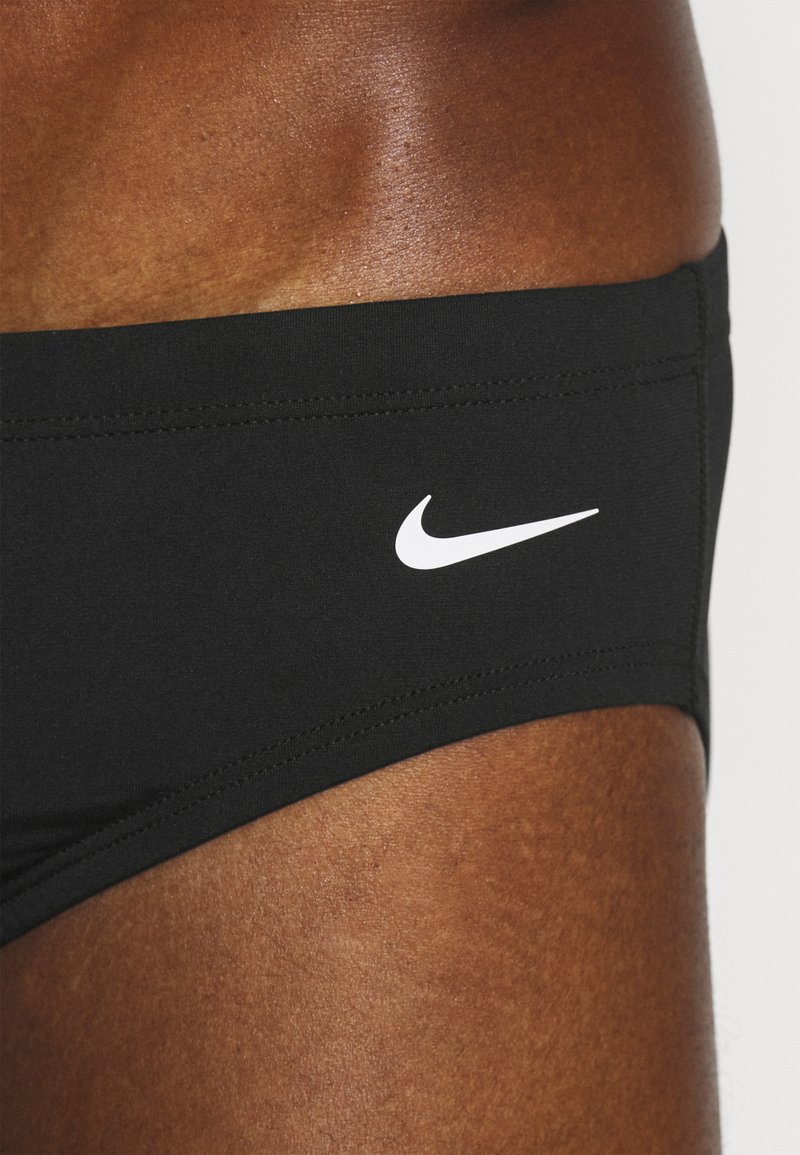 Schwarze Schwimmshorts aus dehnbarem Material mit einem weißen Nike-Logo auf der linken Seite. Sie zeichnen sich durch klare Linien und eine enganliegende Passform aus.