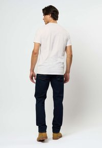 Valkoinen lyhythihainen t-paita, joka on yhdistetty tummansinihin farkkuihin, joissa on suora lahje ja huomaamaton ommel takataskuissa. Beige kengät.