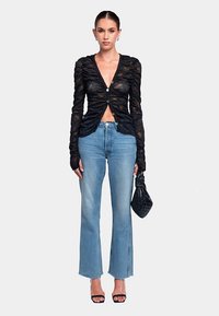 Top nero a maniche lunghe arricciato con chiusura a bottoni, abbinato a jeans a zampa di colore azzurro chiaro. Gli accessori includono una piccola borsa nera.