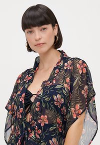 Blomstrende kimono-stil dekke i lett, gjennomsiktig stoff. Mørkeblå bakgrunn med rosa og grønne blomster mønster. Åpen frontdesign og avslappede ermer.