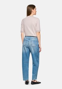 Helles pinkes T-Shirt mit kurzen Ärmeln, kombiniert mit hochgeschnittenen, hellblauen Jeans. Die Jeans haben eine lockere Passform und zwei hintere Taschen. Schwarze flache Schuhe.