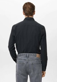 Czarna koszula na guziki wykonana z gładkiego materiału, z klasycznym kołnierzykiem i długimi rękawami, zestawiona z wyblakłymi szarymi dżinsami z tylnymi kieszeniami.