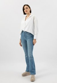 Bílá košile s dlouhým rukávem, spárovaná se světle modrými rozšířenými džíny a béžovými platformovými teniskami. Minimalistický design s uvolněným střihem.