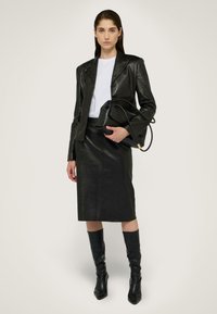 Schwarze Lederjacke mit satinierter Oberfläche, kombiniert mit einem Bleistiftrock, knielangen schwarzen Stiefeln und einer lässigen schwarzen Handtasche.