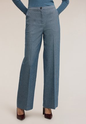 Szerokie spodnie w teksturowanej niebieskiej tkaninie, z zapięciem na guzik i fałdami z przodu. Połączone z burgundowymi szpilkami.