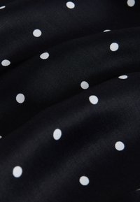 Fekete szövet sima textúrával, egyenletesen elhelyezkedő apró fehér pöttyökkel, finoman redőzött formában.