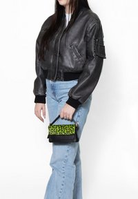 Giacca bomber nera in pelle con polsini a coste, abbinata a jeans dritti azzurri e una piccola borsa nera con stampa leopardata verde.