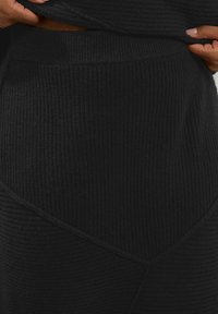 Musta ribattuja neulehame korkealla vyötäröllä, jossa on vinosauma ja tekstuurikangas lisättyyn yksityiskohtaan.