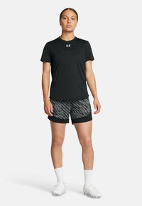 Svart kortärmad t-shirt med en vit logotyp och mönstrade shorts i svart och grått. Vita sportstrumpor och fotbollsskor. Enkelt design, atletisk passform.