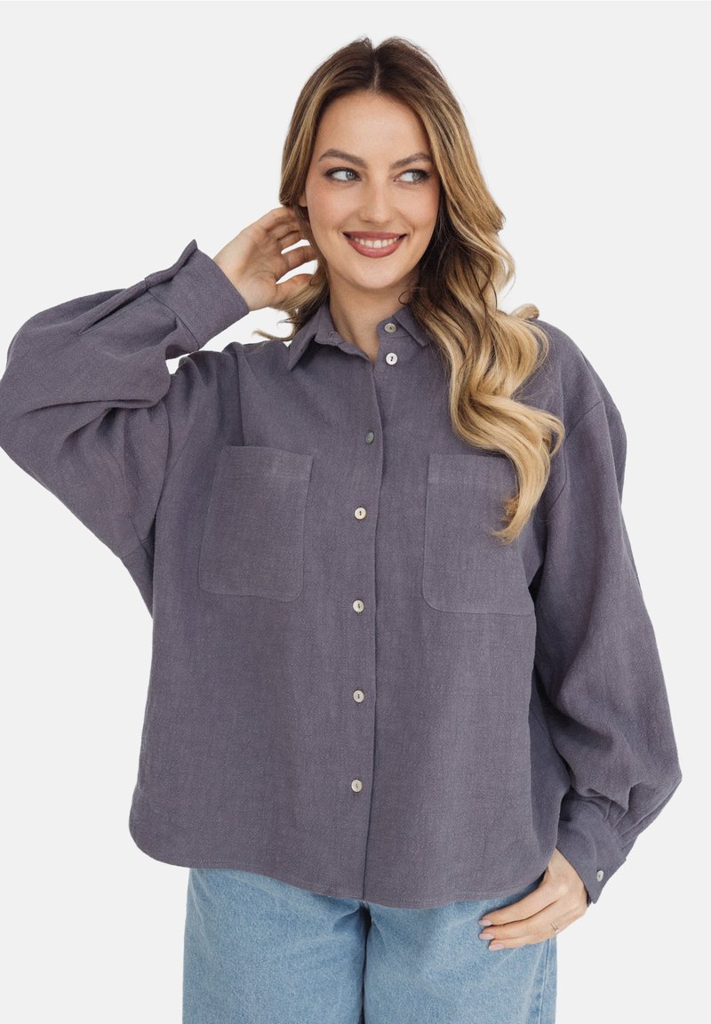Koszula z długim rękawem, zapinana na guziki, wykonana z miękkiego, teksturowanego materiału w kolorze lawendy. Posiada dwie kieszenie na piersi i luźny krój, z zaokrąglonym dołem.