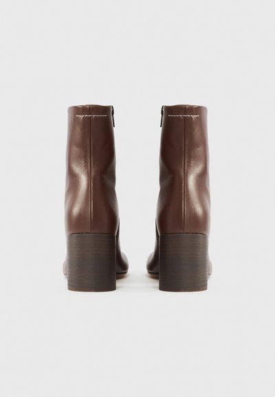 Brūnas ādas potītes zābaki ar gludu virsmu, blokpapēdi un sānu rāvējslēdzēju. Šuves detaļa gar augšējo malu.