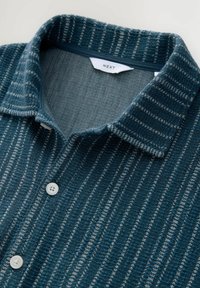 Striped knit shirt in teal and gray with a collared neckline, featuring white buttons and a textured fabric. Brand label visible inside collar.