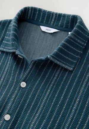 Button-up shirt featuring a textured fabric with green and white vertical stripes, a soft collar, and two white buttons at the front.