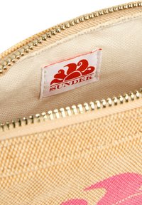 Pochette zippée en tissu beige avec une finition texturée. L'intérieur présente une étiquette blanche avec un logo rouge et un design rose en accent. Fermeture éclair dorée.