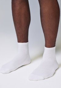 Fehér pamut boka zokni bordázott szegéllyel, sima textúrával és megerősített orr- és sarokrészekkel, barna lábakon fényes háttér előtt viselve.