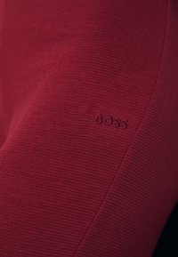 Rød ribbestrikket genser med en tonal hevet "BOSS" logo på ermet. Laget av et mykt, strukturert stoff.