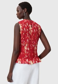 Top peplum rosso floreale con tessuto textured, design senza maniche, apertura a chiave sul retro e dettaglio di orlo arricciato.