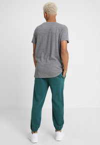 Tricou scurt gri cu hem curbat, asociat cu pantaloni joggeri teal. Pantalonii au un talie elastică și gleznă răsucită.
