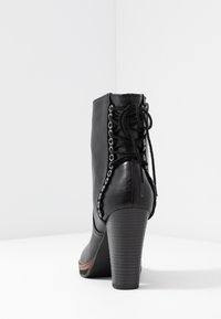 Stivale alla caviglia in pelle nera con design a lacci, caratterizzato da occhielli metallici e un tacco testurizzato, messo in risalto da una piattaforma in legno.
