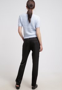 Maglione corto a maniche corte di un azzurro chiaro e morbido con dettagli a frange, abbinato a pantaloni neri fit e scarpe slip-on nere. Vista posteriore mostrata.