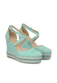 Sandales à talon compensé vert menthe avec une finition en daim, dotées de brides de cheville croisées, de bouts texturés et d'un accent de perles sur la semelle.