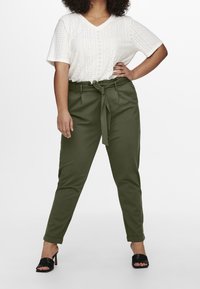 Vit ögonlapp v-ringad topp med korta ärmar, ihopparad med olivgröna tapered byxor med knyt i midjan. Svarta klacksandaler med bred rem.