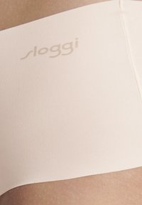 Beige Sloggi seamless slip, geribbelde textuur, mid-rise ontwerp, zachte stof. Bevat subtiele branding op de tailleband.