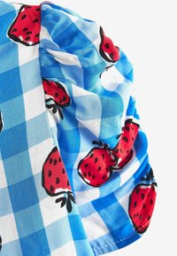 Tissu à carreaux bleu et blanc avec des imprimés de fraises rouges, montrant des plis et une texture douce.