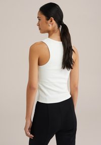 Hvid, ribbet tanktop med en tætsiddende form, der har brede ærmehuller og en cropped længde, parret med sorte tætsiddende bukser.
