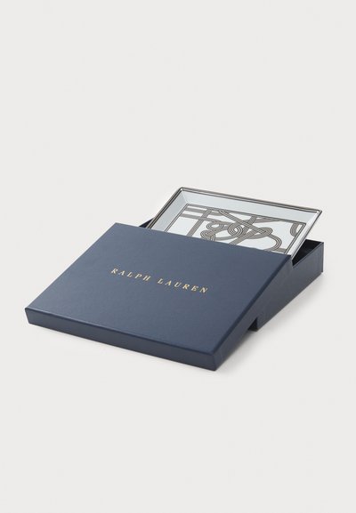 Laatikko lahjaksi tummansinisellä värillä, jossa on kultainen teksti "Ralph Lauren", sisältää neliön muotoisen lasialustan, jossa on ohut musta viivakuviomalli. Alustan reunassa on hopeinen kehys.