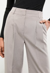 Pantalones de cintura alta con diseño de frente plisado, que cuentan con un patrón en blanco y negro, fabricados con una tela ligera.