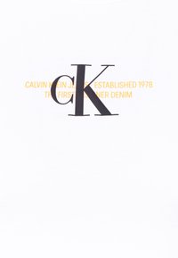 Large black "ck" logo over yellow text reading "Calvin Klein Jeans - Established 1978 The First Designer Denim" on white fabric.
